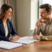 Une femme et un homme discutent sereinement d’un ajustement tarifaire autour de dossiers contractuels vierges et d’une balance symbolisant l’équilibre commercial.